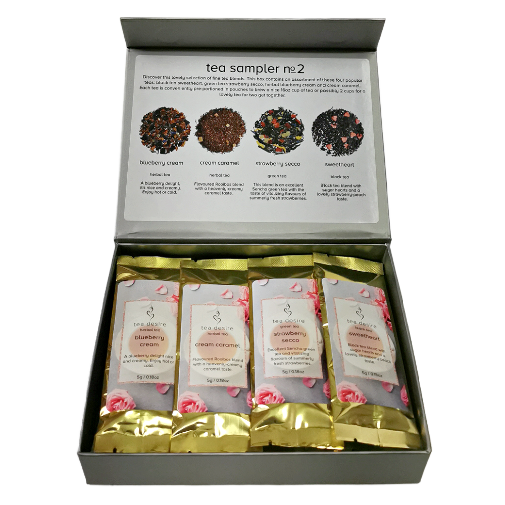 An open gray gift box containing four individually wrapped tea bags. The inner lid is printed with a tea sampler description and four circular tea blend images labeled blueberry cream, cream caramel, strawberry seco, and sweetheart.