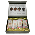 An open gray gift box containing four individually wrapped tea bags. The inner lid is printed with a tea sampler description and four circular tea blend images labeled blueberry cream, cream caramel, strawberry seco, and sweetheart.