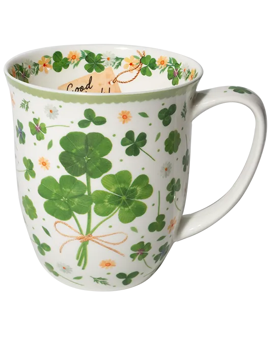 White mug with green four-leaf clovers tied in a bouquet, small flowers, and a pale green rim.