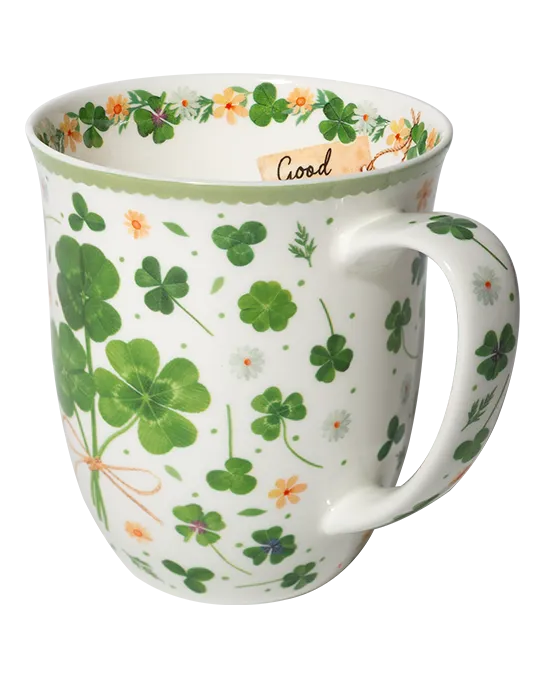 White mug with green four-leaf clovers tied in a bouquet, small flowers, and a pale green rim.