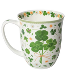 White mug with green four-leaf clovers tied in a bouquet, small flowers, and a pale green rim.