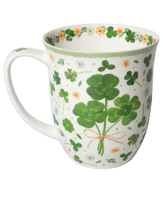 White mug with green four-leaf clovers tied in a bouquet, small flowers, and a pale green rim.