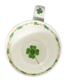 White mug with green four-leaf clovers tied in a bouquet, small flowers, and a pale green rim.