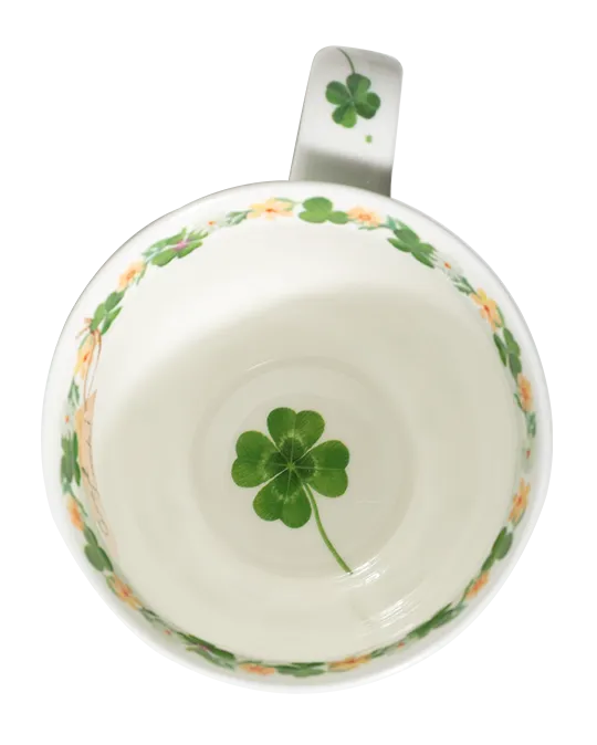 White mug with green four-leaf clovers tied in a bouquet, small flowers, and a pale green rim.