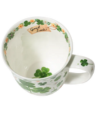 White mug with green four-leaf clovers tied in a bouquet, small flowers, and a pale green rim.