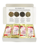 A white cardboard tea sampler box labeled 'tea sampler no 5' with four individual tea sachets arranged in the open tray. The inside lid shows four labeled tea blends with photos and names: Tulsi Lemon, Japanese Cherry, London Truffle, and  Mountain Herbs.