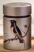 Silver cylindrical container with a bird illustration on a branch